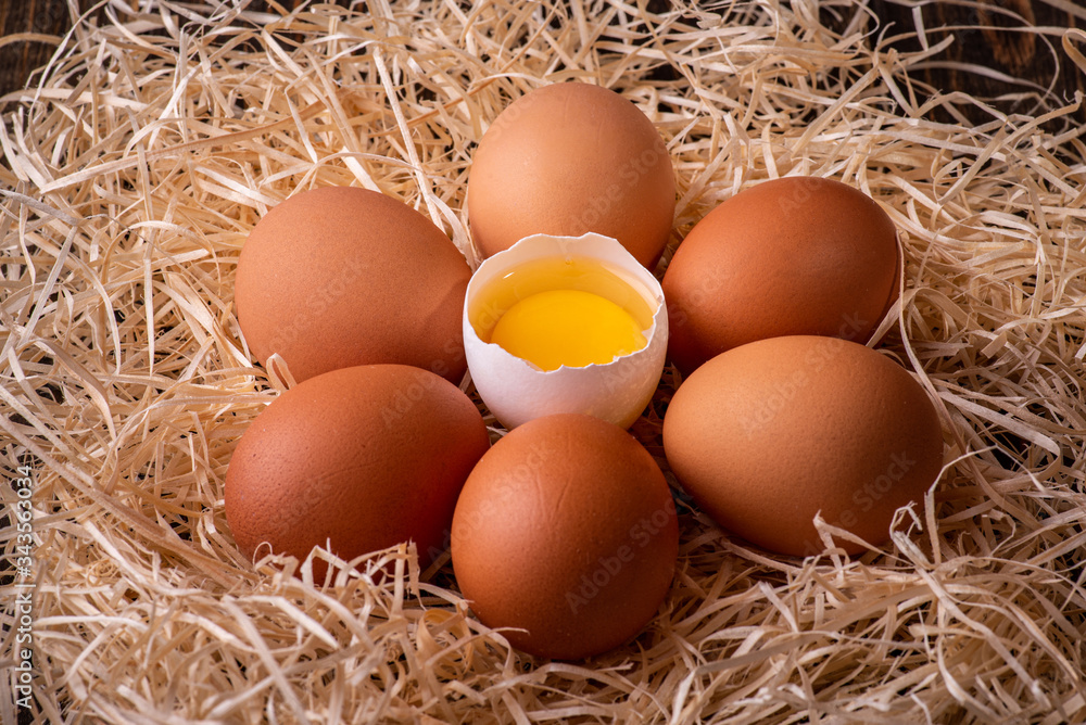 Fresh chicken eggs in a nest of hay on a wooden background.