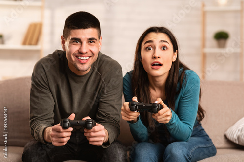 Young couple sitting on couch playing video games at home