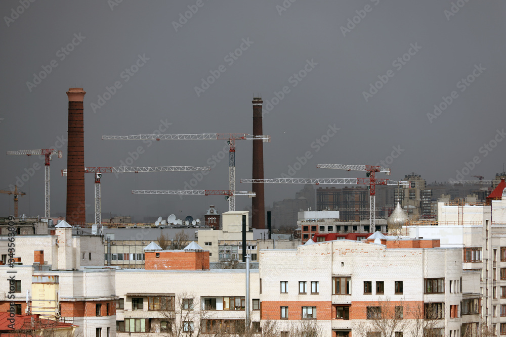 industrial landscape, construction cranes and pipes of plants against a dark sky, environmental pollution