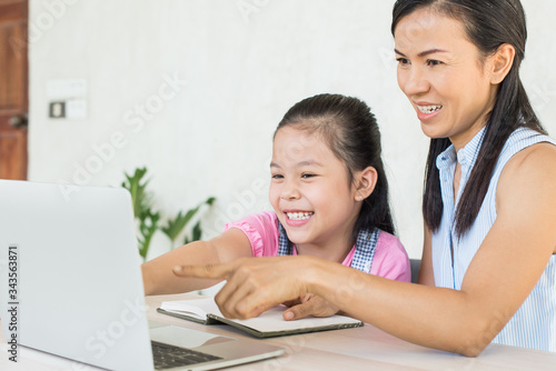 asia girl student online learning study online video call teacher. social distance during quarantine, self-isolation, online education concept, homeschool, cute girl with mother doing homework at home