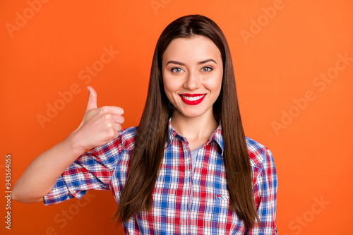 Photo of attractive lady bright red pomade toothy smile raise thumb finger up approving good product quality wear casual plaid shirt isolated vibrant orange color background