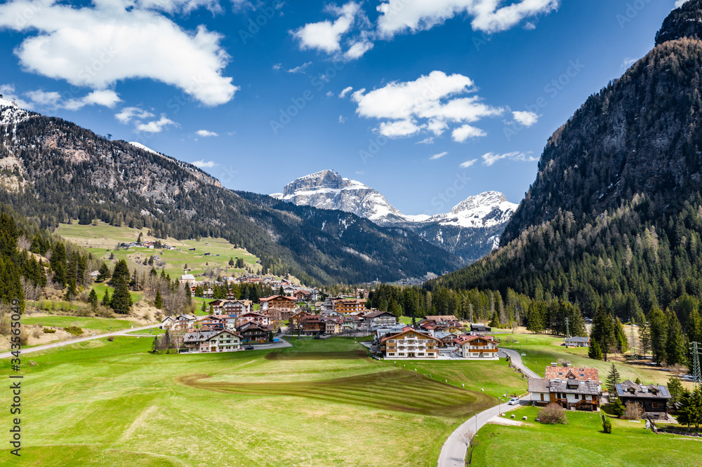 Aerial view of valley with Chalet, green slopes of the mountains of Italy, Trentino, Fontanazzo, huge clouds over a valley, roofs of houses of settlements, green meadows, Dolomites on background,