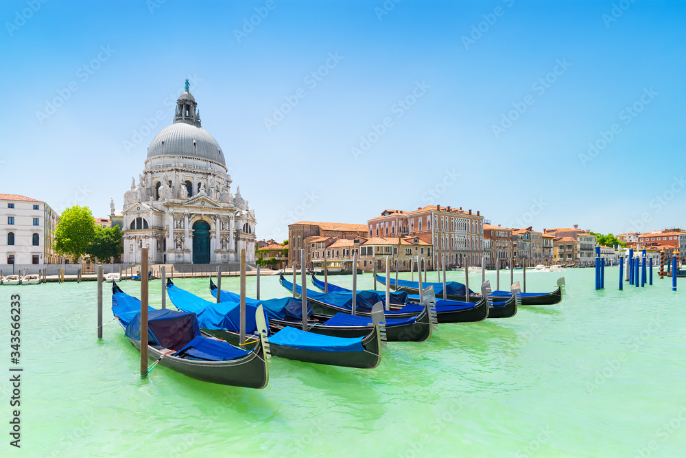 Panoramic beautiful  view of traditional venetian gondolas moored in water of Grand Canal in front of Basilica di Santa Maria della Salute church, Venice, Italy, in bight sunny day