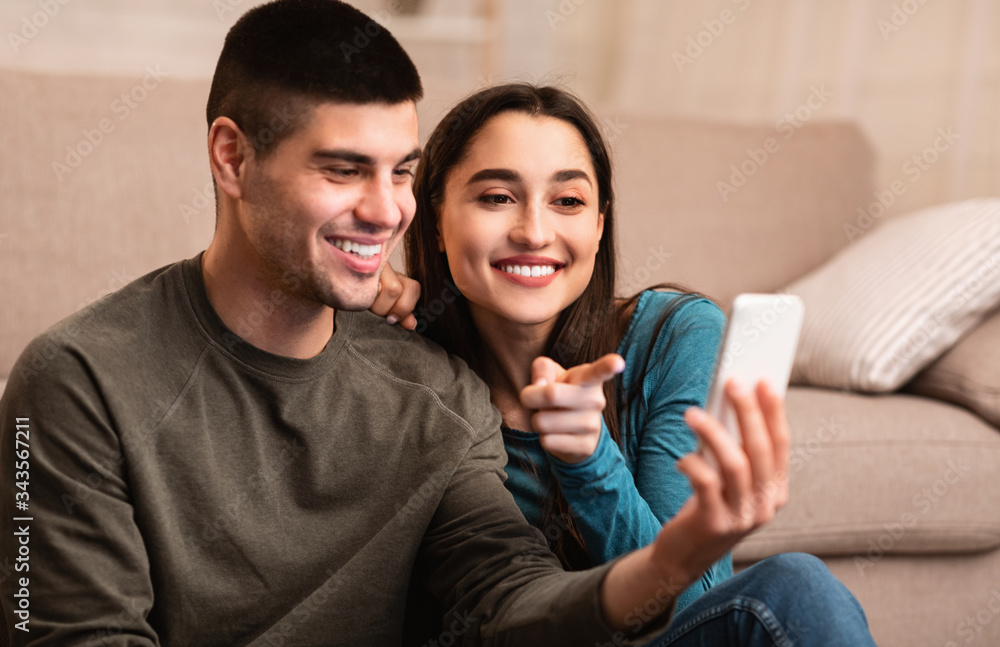 Couple using cell phone sitting on floor Couple using cell phone sitting on floor