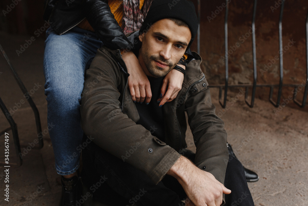 Obraz premium Handsome man with beard sitting on the road and woman hands on his shoulders