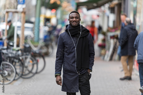 Black Man with Earphones and Winter Coat Smiling on Street