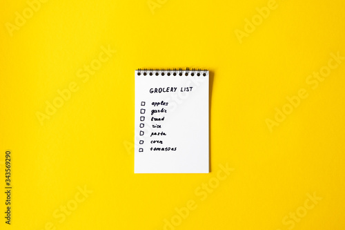 Grocery list paper notepad on yellow background with copy space, top view