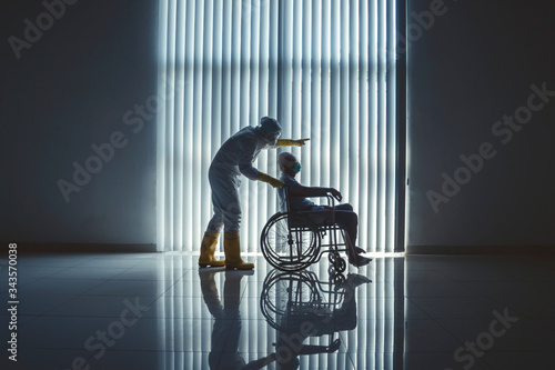 Doctor with hazardous materials suit pushing an elderly patient in wheel chair