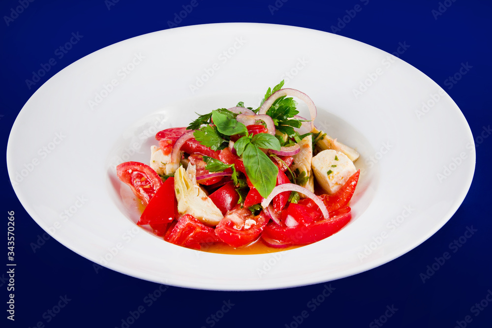 Vegetable salad of tomatoes, peppers, artichokes and onions on a white plate on a blue background. Vegetable salad of tomatoes, peppers, artichokes and onions on a white plate on a blue background.