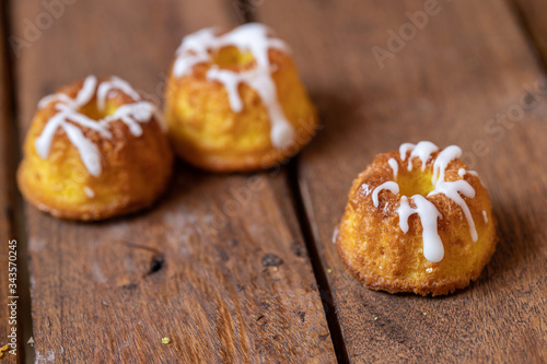 kleiner gelber kuchen bzw gugelhupf aus zitronen mit zuckerguss auf braunem tisch aus brettern und holz