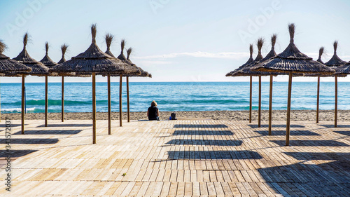 Fototapeta Naklejka Na Ścianę i Meble -  Mujer sola sentada en la playa junto a un grupo de parasoles en Fuengirola
