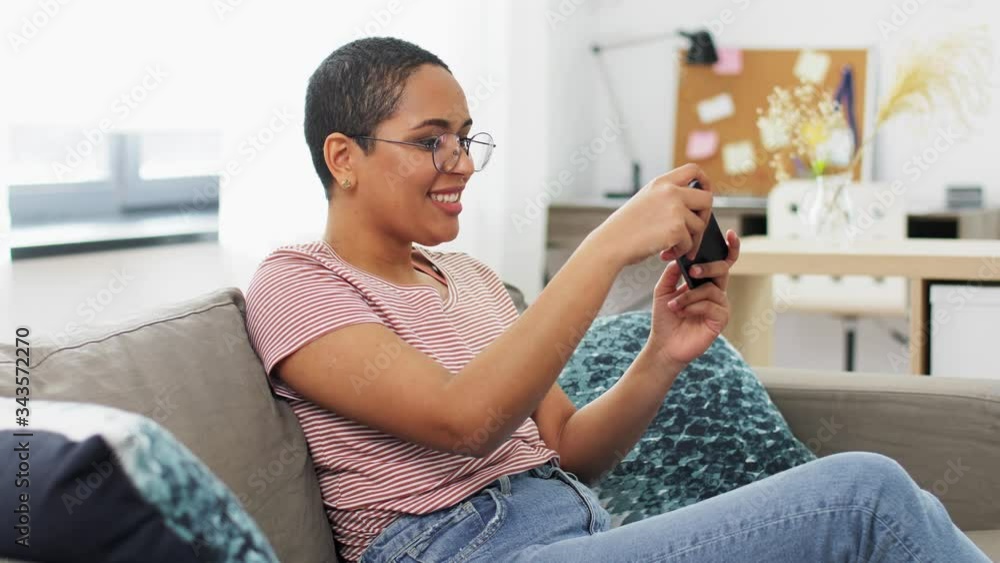 technology and people concept - smiling african american woman in glasses with smartphone playing game at home technology and people concept - smiling african american woman in glasses with smartphone playing game at home