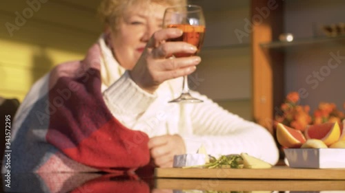 Senior woman sitting on the porch of a country house with glass of wine in her hands. Spring, the evening sun beautifully illuminating wine glass.