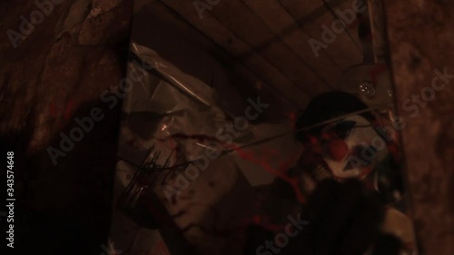 A scarier clown with knife at crude basement with a mirror on the wall