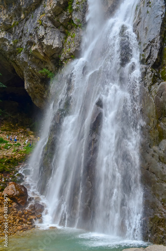 Gega waterfall in the mountains of Abkhazia. A group of tourists next to that. It is located in the northern spurs of the Gagra Range at an altitude of 530 meters above sea level.