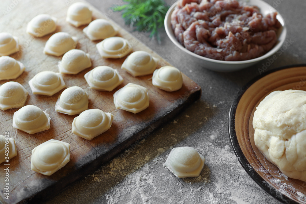 The process of making homemade dumplings with meat, russian national dish: meat for filling in a bowl, dough, and raw dumplings on a wooden board on the gray table The process of making homemade dumplings with meat, russian national dish: meat for filling in a bowl, dough, and raw dumplings on a wooden board on the gray table