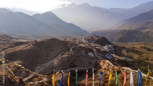 Prayer flags waving above Himalayan village, Muktinath, along Annapurna Circuit Trek in Nepal. There are only a few buildings. In the back there is a high, snow capped Himalayan chain. Spirituality