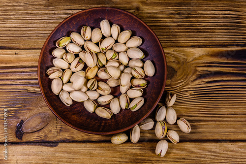 Ceramic plate with pistachio nuts on a wooden table. Top view