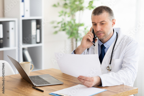 Male doctor with medical report calling on phone at clinic