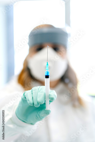 A hand holding a syringe with protective gloves with the face of the medical background