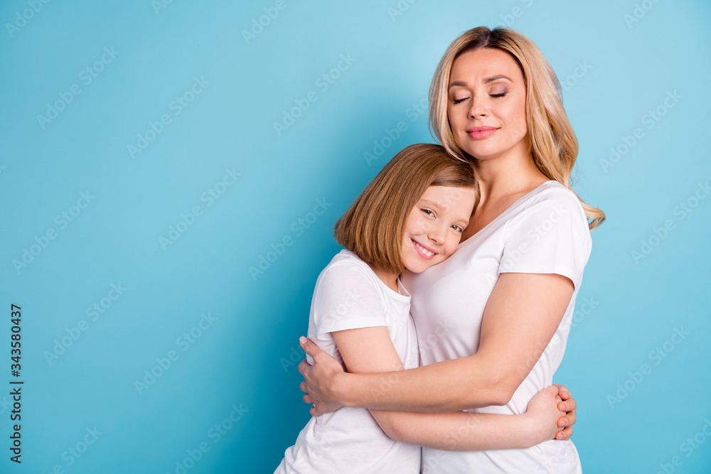 Profile photo of two people young beautiful mom lady small little daughter blonds hugging eyes closed hold hands wear casual white s-shirts isolated blue color background Profile photo of two people young beautiful mom lady small little daughter blonds hugging eyes closed hold hands wear casual white s-shirts isolated blue color background