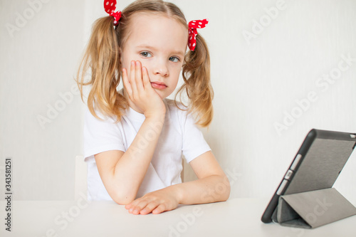 Little girl is talking online. Home schooling. Distance learning. Online call to friends.