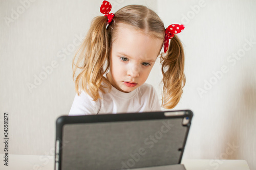 Little girl is talking online. Home schooling. Distance learning. Online call to friends.