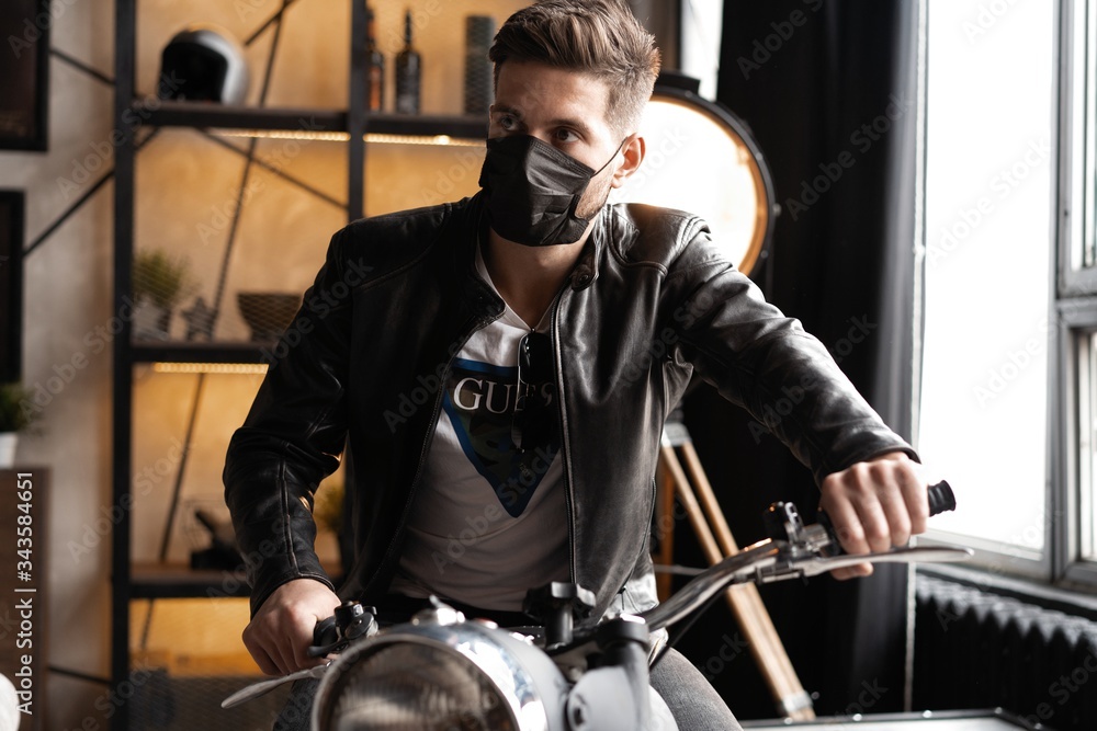 Fototapeta premium Handsome brutal male biker in black mask in leather jacket sitting on motorcycle looking forward.