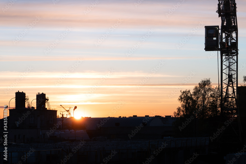 Evening outline of the city. The silhouette of the factory against the sky or sunset. The tower crane operates on the territory of the factory. Evening outline of the city. The silhouette of the factory against the sky or sunset. The tower crane operates on the territory of the factory.