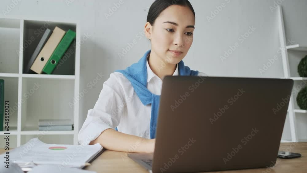 A calm positive young asian secretary woman sitting at the table and working on laptop computer while working in office A calm positive young asian secretary woman sitting at the table and working on laptop computer while working in office