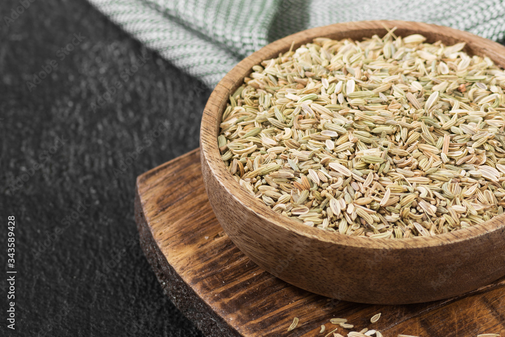 Dried fennel in a wooden bowl on the black kitchen table Dried fennel in a wooden bowl on the black kitchen table