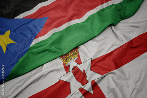 waving colorful flag of northern ireland and national flag of south sudan.