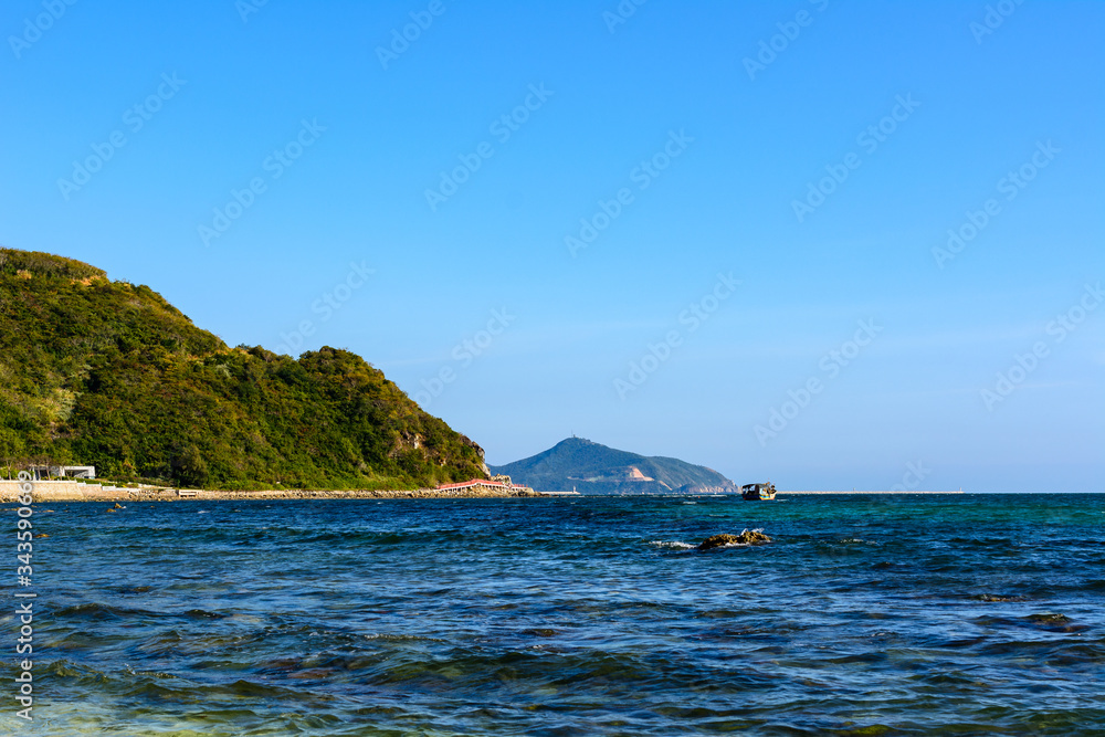 Sunny day, sand, clear turquoise sea, coral reefs on the coast of Xiaodonghai Bay in South China Sea. Sanya, island Hainan, China.