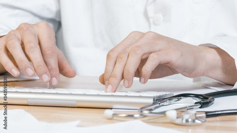 Fototapeta premium Hands of Doctor typing on keyboard of computer with stethoscope in a clinic, close up.