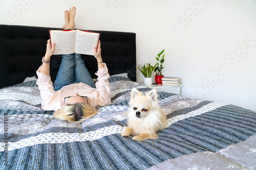 Foto Blonde hair woman sitting on cozy bed with dog, holding open book and reading