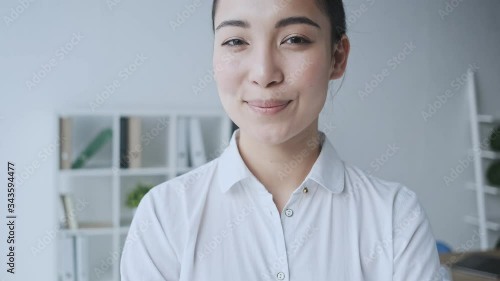 A charming happy calm young asian businesswoman is looking and smiling to the camera while sitting in the office A charming happy calm young asian businesswoman is looking and smiling to the camera while sitting in the office