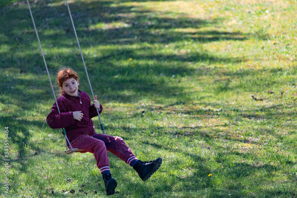 Bambina sorridente con capelli rossi lunghi su una altalena di un parco, bellezza, giovinezza e fashion per messaggi e comunicazioni di moda su riviste e magazine