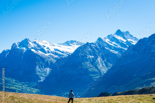 Φωτογραφία Man standing alone in a meadow facing the Swiss Alps