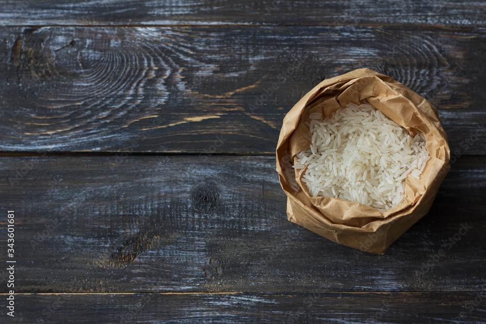 Raw white long-grain basmati rice in a craft bag on a wooden background, top view, space Raw white long-grain basmati rice in a craft bag on a wooden background, top view, space