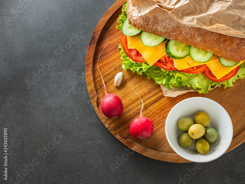 close up view to vegetarian ciabatta with radish and olives on wooden plate and dark background