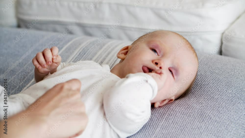 Sweet adorable baby lying on couch and biting her fingers. New mother nursing six month child at home. Cropped shot of hands. Childhood concept Sweet adorable baby lying on couch and biting her fingers. New mother nursing six month child at home. Cropped shot of hands. Childhood concept