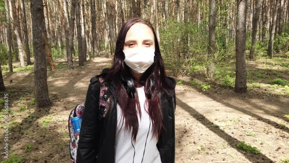 Young woman in medical mask on her face walking in forest on fresh air. Adult female covered her face with mask to protect yourself from diseases. Concept of threat of coronavirus epidemic infection. Young woman in medical mask on her face walking in forest on fresh air. Adult female covered her face with mask to protect yourself from diseases. Concept of threat of coronavirus epidemic infection.