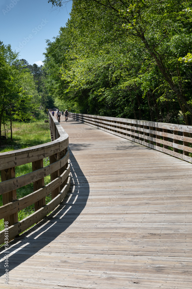 Distant walkers and runners on an elevated wood boardwalk through a nature area, vertical aspect