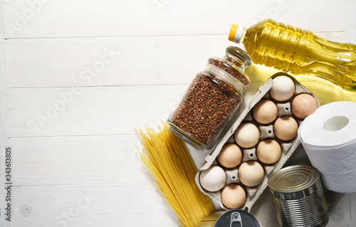 Food donations on a white wooden background: oil, buckwheat, eggs, canned food. Sit at home. Quarantine. Food delivery. photo