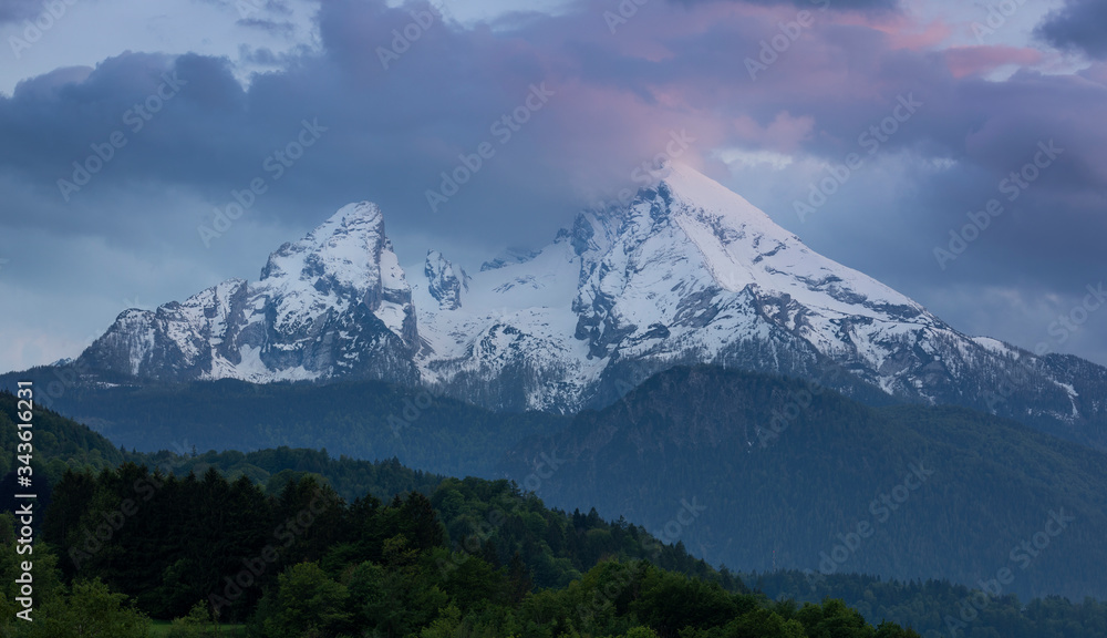 Snow covered mountain peaks of Watzmann at Berchtesgaden with clouds during sunset, green forest in foreground, Bavaria. Snow covered mountain peaks of Watzmann at Berchtesgaden with clouds during sunset, green forest in foreground, Bavaria.