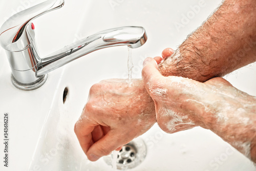 Senior elderly man his hands and wrist under tap water faucet, detail photo. Can be used as hygiene illustration concept during coronavirus / covid-19 outbreak prevention