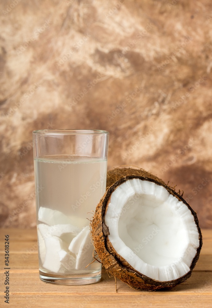 Health content, coconut water in a glass, coconut halves, brown background Health content, coconut water in a glass, coconut halves, brown background