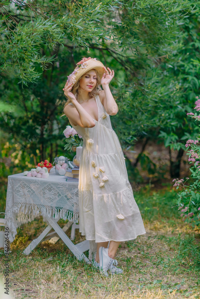 Amazing girl in retro dress holding her flower hat.  Dreamy scene at backyard of country house garden.