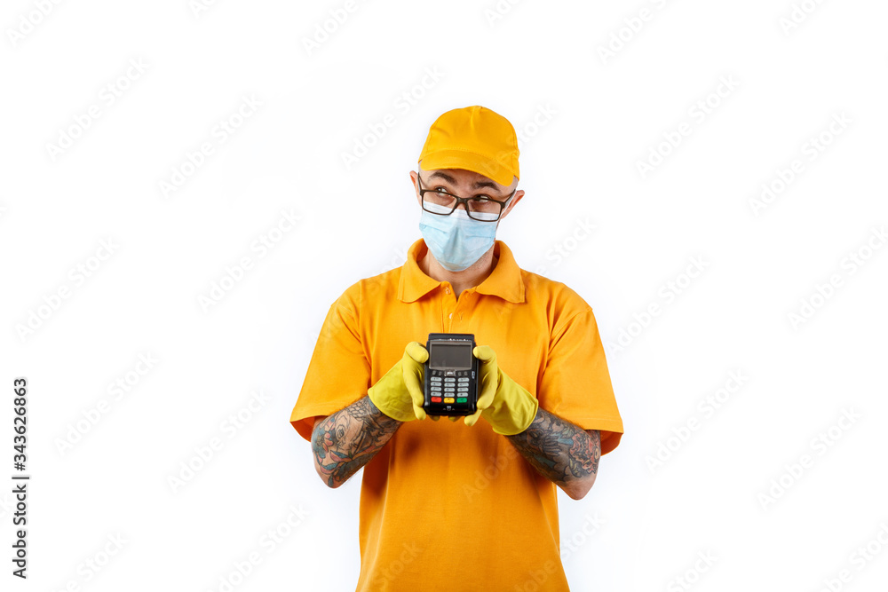 A cautious young man from a courier delivery service in a medical mask and gloves holds a terminal in his hands for cashless payment on a white background A cautious young man from a courier delivery service in a medical mask and gloves holds a terminal in his hands for cashless payment on a white background