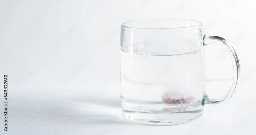 Sparkling tablet throw into a glass transparent glass, the glass is on a white background, a pill for cold of claret color, bubbles rise up, splashes take off from a glass Sparkling tablet throw into a glass transparent glass, the glass is on a white background, a pill for cold of claret color, bubbles rise up, splashes take off from a glass